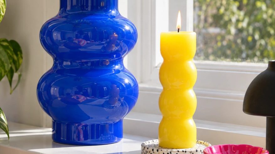 A blue vase, yellow candle and pink dish on a windowsill